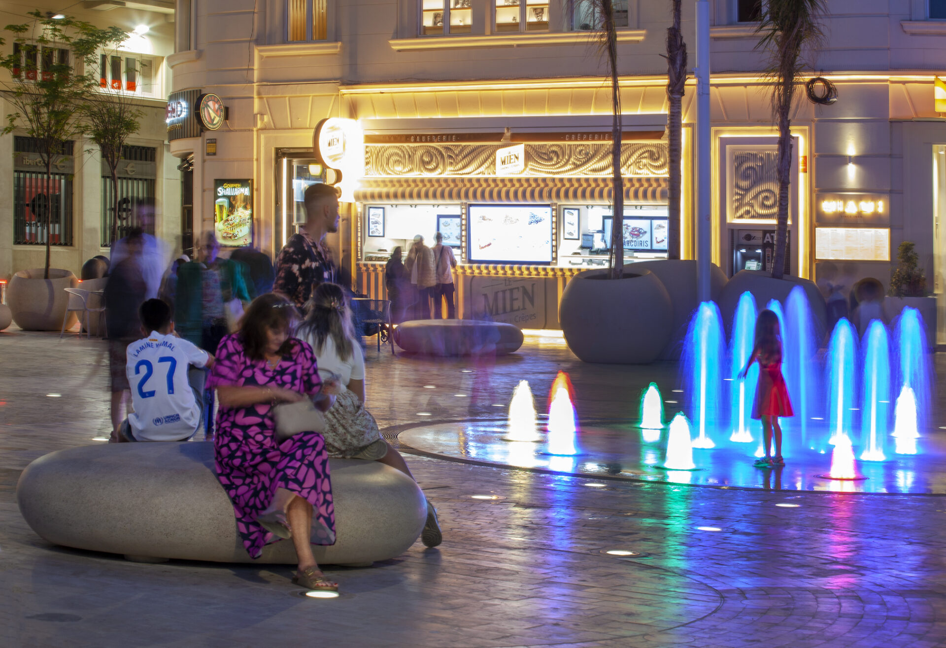 Fuente ornamental con colores y bancos redondeados con gente sentada